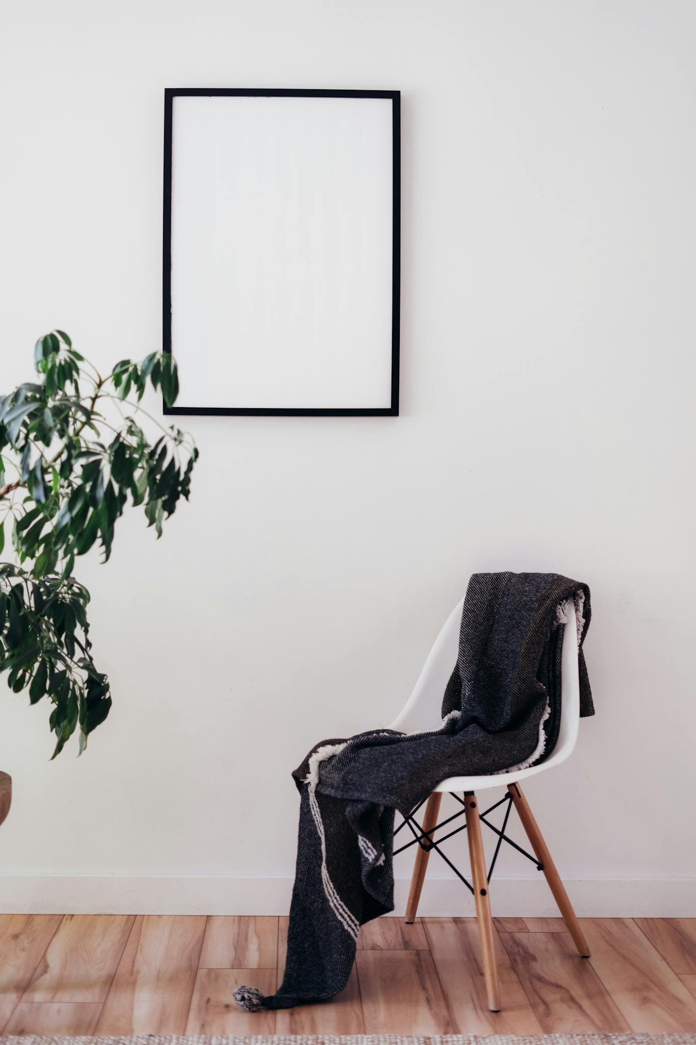 A cozy modern room with a chair, houseplant, and blank picture frame on white walls.